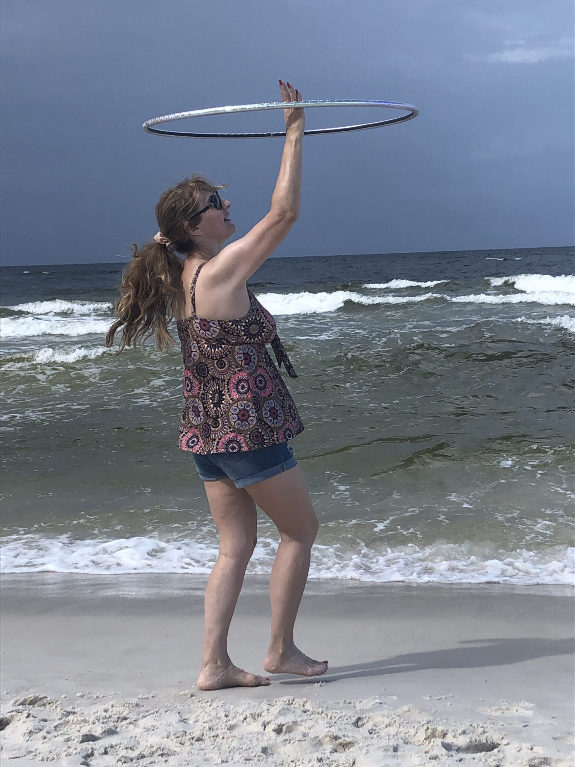 Woman spinning hula hoop on sandy beach